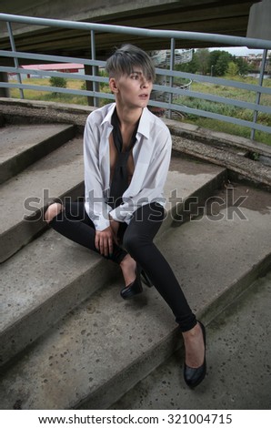 Young woman model in manly style wearing in shirt sit on stairs.