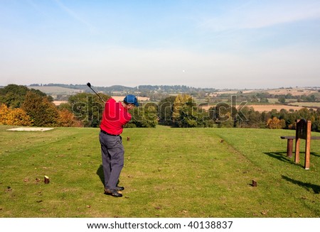 A young male golfer teeing off on an autumn morning on a golf course in England. Slight motion blur on the clubhead. Tee shot heading straight down the fairway.