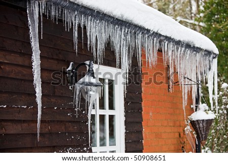 Icicles hanging from a lamp on the exterior of a panelled wooden house with a white windowed door. Photo has relatively short depth of field, with focus on the lamp covered with icicles.