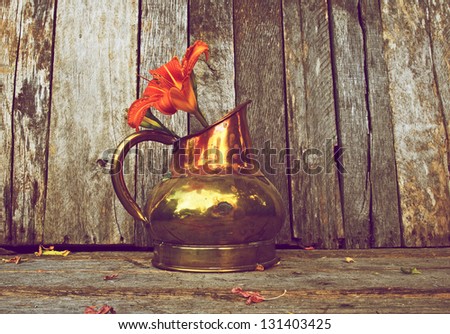 Lily flower in an antique copper vase on a rustic wood backdrop with copy space, wide angle.