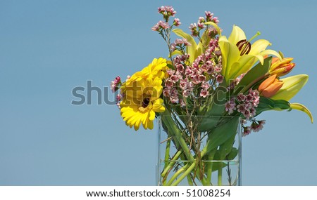 Spring flowers in a glass vase against a brilliant blue sky with room for text.