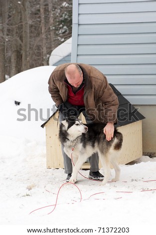 A middle aged man stops to pet a neglected Shepard husky mix dog on a native reservation after delivering a donated dog house to him.