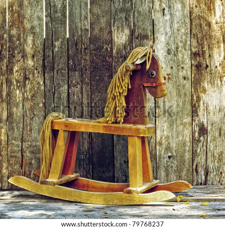 Old rocking horse in the partial shade on a rustic country backdrop.