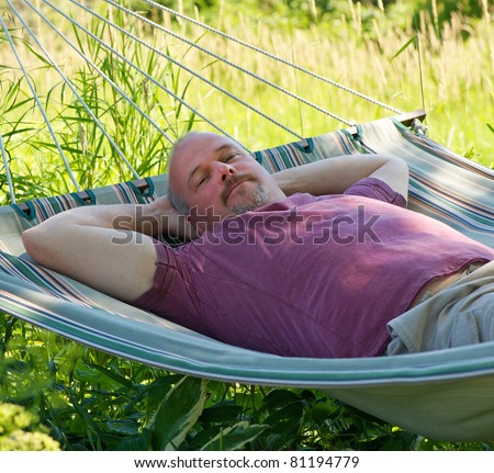 Close up portrait  of a middle aged man happily relaxing in a hammock in the shade on a summer day.