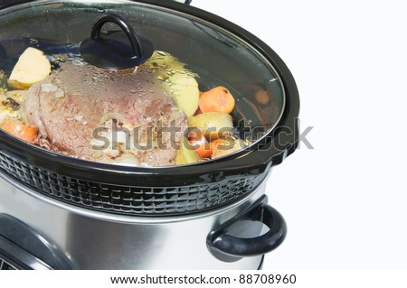Crock pot with a lightly browned seasoned blade roast with golden potatoes and chopped carrots simmering, isolated on white with copy space.