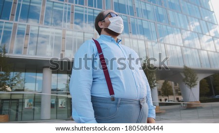 Overweight office employee tired of wearing safety mask outdoors. Portrait of obese businessman standing near office building in facial mask Сток-фото © 