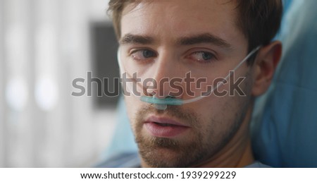 Upset man lying with oxygen nasal catheter on face preparing for surgery. Close up portrait of sick young male patient with nasal tube lying in hospital bed Foto stock © 