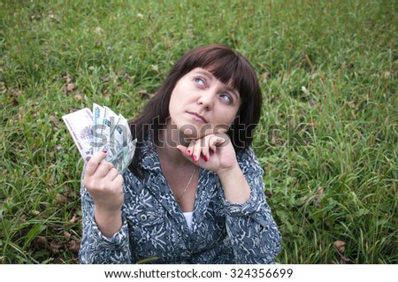 Girl holding a money and thinks on a green lawn