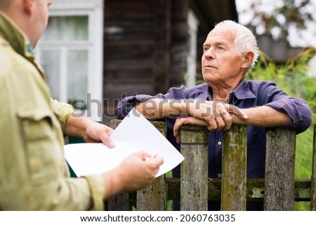 Grandfather talking to census agent standing at the fence of his country house Stockfoto © 
