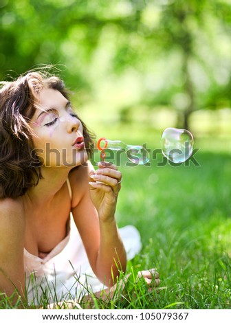romantic young girl inflating colorful soap bubbles in summer park