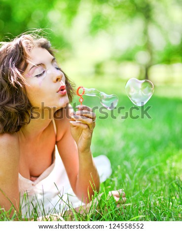 romantic young girl laying and inflating colorful soap bubbles in spring park