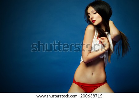 Portrait of beauty attractive fashion slim healthy young woman dancing with perfect training sexy tanned skin sport body in an ideal white and red lingerie on dark blue background