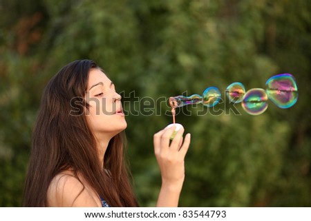 portrait of attractive young girl inflating colorful soap bubbles outdoor