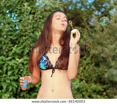 Beauty young woman in cute swimsuit inflating soap bubbles