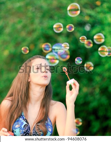 Beautiful young woman inflating colorful soap bubbles in pure nature