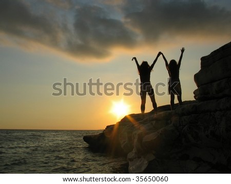 Female silhouettes on seacoast against the sunset sky