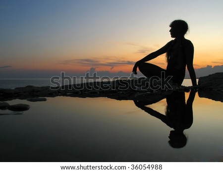 Female silhouette on seacoast against the sunset sky