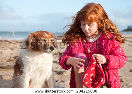 little red haired girl dressing up her dog in her winter hat on a beach