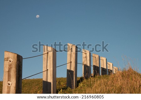 fence line on a hill with blue sky and moon rising