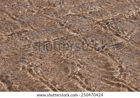 patterns on the surface of a shallow tidal stream running over sand out to sea