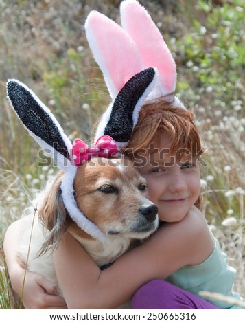 little red haired girl with her pet dog dressed up as Easter bunny on an easter egg hunt in meadow of bunnies tail grass