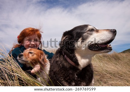 little red haired girl playing with her pet dog in dune grasses on a sunny day