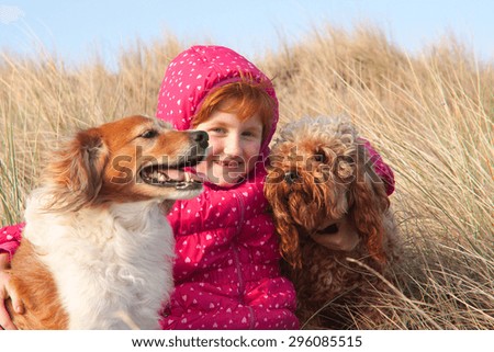 red haired girl in winter jacket hugging red haired collie type dog on a cold winter\'s day in grassy sand dunes at a beach in Gisborne, New Zealand
