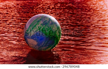 concept image for global environmental issue using inflatable rubber ball with earth like markings and blood colored  rippled water surface
