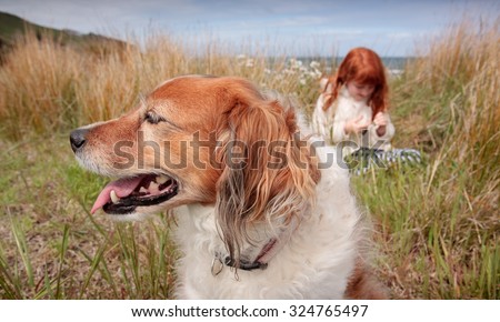 little red haired girl with red haired collie type dog sitting among long dune grass on a sand dune at a surf beach, near Gisborne, East Coast, North Island, New Zealand