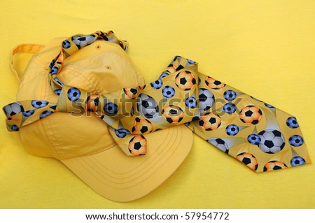 Yellow baseball cap and tie with soccer balls on it against yellow background