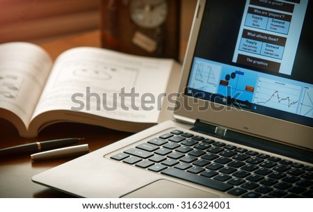 Laptop with diagrams , book , pen and  clock at office desk. Shallow depth of field. Warm light balance.