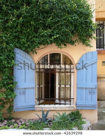 Arched window with blue shutters and wrought-iron bars in medieval village of Mougins, France.