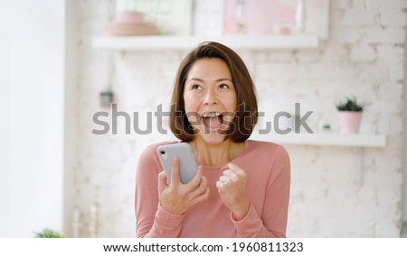 Young multi ethnic asian woman feel excited celebrating bid win success victory looking at smartphone, excited girl screaming yes winning online game app on cell phone sit on sofa at home