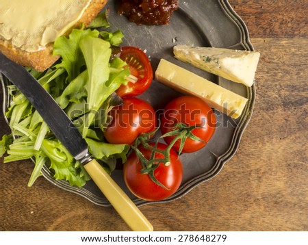 Ploughmans lunch with cheese, a bread roll sliced with butter, tomatoes, lettuce on a vintage pewter plate. Shot from above.