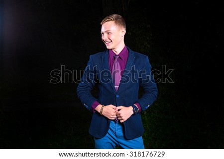 Young handsome man in black suit laughing against black background