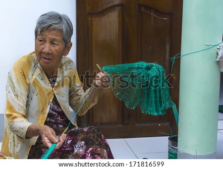 MUI NE, VIETNAM - CIRCA MARCH 2012: Really old lady weaves green fishing net in front of her home.