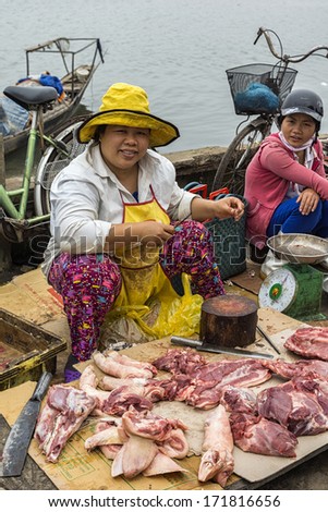 DONG HOI, VIETNAM - CIRCA MARCH 2012: Couple of female butchers at open air market sitting with pieces of meat. At the bay shore displaying fresh cut raw meat on carton in the dirt.