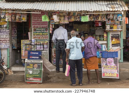 THIRUVANNAMALAI, INDIA - CIRCA OCTOBER 2013: Newspapers and Magazines for sale at small street shop. The dominant language in print is Tamil. Three locals line up to buy.