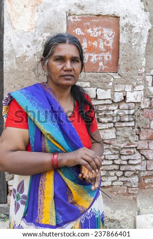 BITHOOR, INDIA - MARCH 2, 2011: This graying woman, dressed in a colorful blue, yellow sari over a red T-shirt holds a cup and an incense stick in her hands.