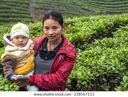 BAC HA, VIETNAM - MARCH 11, 2012: A young mother holds her baby in her arms, standing in the middle of a tea plantation.