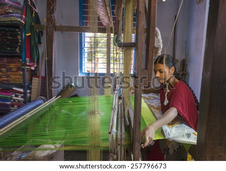 KUMBAKONAM, INDIA - OCTOBER 11, 2013: Home silk sari weaving on a hand loom set in a small room. The young woman works on a green piece of textile.