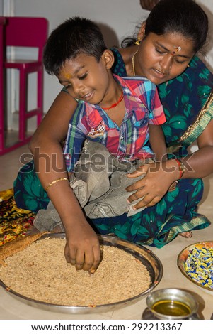 Thanjavur, India - October 14, 2013: Vijayadasam ceremony at the start of school year in Annai Fathima Primary School. Boy writes A in grain. His mother helps him.