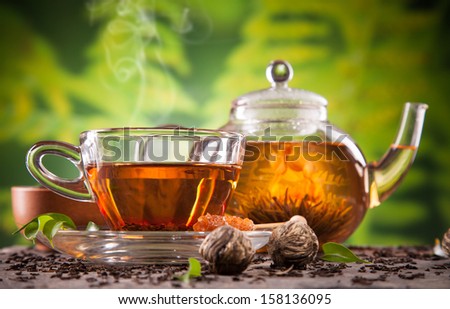 Cup of tea and teapot with blooming tea on blur green background
