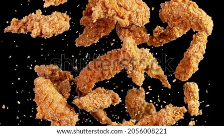 Freeze motion of flying pieces of fried chicken pieces on black background. Concept of levitating food.