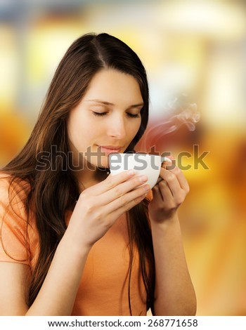 Attractive young brunette woman holding cup of coffee and enjoying smell of drink