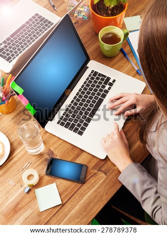 Young woman working with laptop placed on wooden desk with blank screen for text. Shot from aerial view
