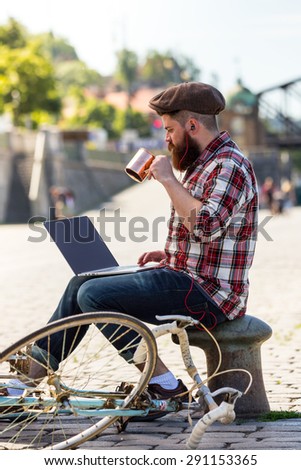 Trendy hipster young man with modern laptop. sitting on sidewalk