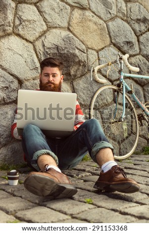Trendy hipster young man with modern laptop. sitting in front of stone wall