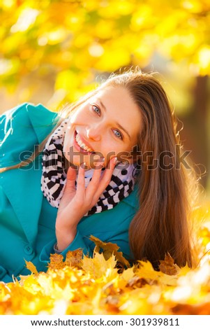 Beautiful brunette girl lying in autumn leaves with smilling face. Concept of happiness and joy