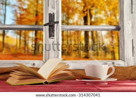 Vintage wooden window overlook autumn trees, shot from cottage interior with cup of coffee and book